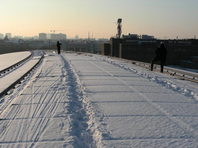 Ein Industriekletterer von ZITRAS in schwarzer Jacke steht auf verschneiten Gleisen und führt Winterdienstarbeiten durch, wie Schneebeseitigung und Eiszapfenentfernung.