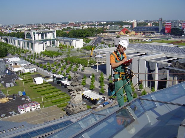 Ein Mann in Sicherheitsausrüstung steht auf einem Dach und notiert etwas auf einem Klemmbrett.