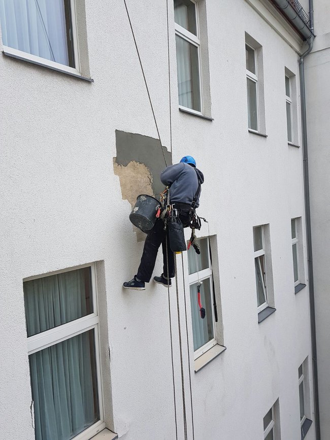 Ein Industriekletterer von ZITRAS führt Verputzarbeiten an einer Gebäudefassade durch.