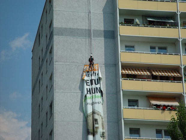 Industriekletterer von zitras bei der Montage eines großen Banners an einem Gebäude in einem urbanen Umfeld