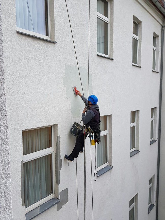 Ein Industriekletterer von ZITRAS führt Verputzarbeiten an einer Gebäudefassade aus
