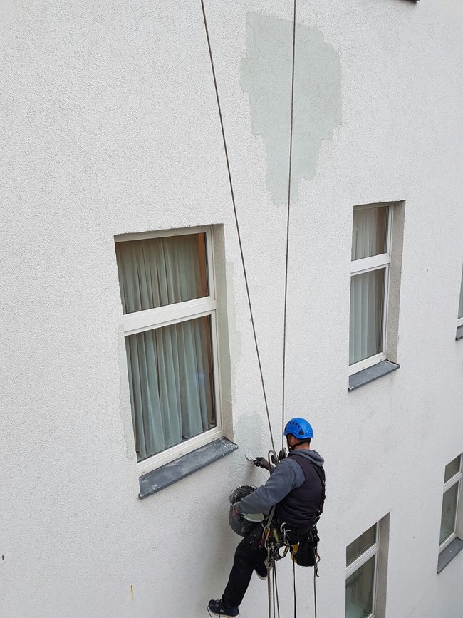 Ein Industriekletterer von ZITRAS führt Verputzarbeiten an einer Fassade durch.