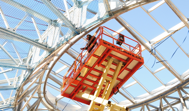 Ein ZITRAS-Mitarbeiter montiert auf einer Plattform eines Hubsteigers ein Personenauffangnetz an einer Metallstruktur.