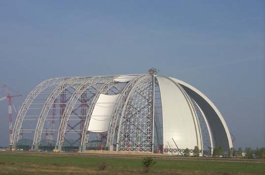 Eine große weiße Kuppelkonstruktion mit einem Metallrahmen vor einem wolkenlosen blauen Himmel.