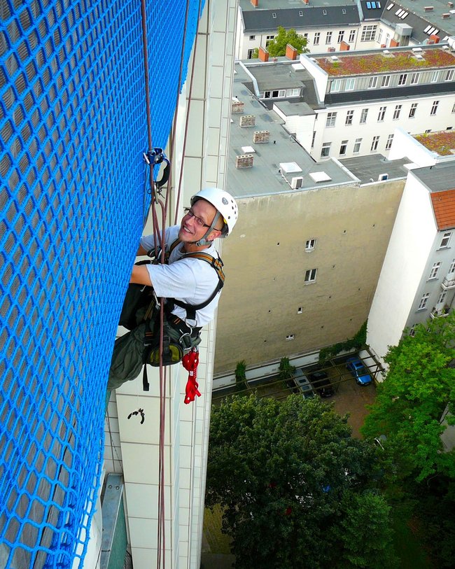 Person in Kletterausrüstung an einem hohen Gebäude.