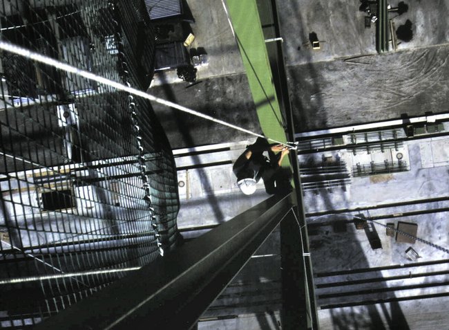 Person mit Schutzhelm klettert auf einer schmalen grünen Stahlstruktur.