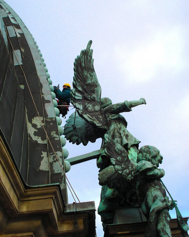 Arbeiter mit Sicherheitsausrüstung klettert am Berliner Dom, Engelsskulptur im Vordergrund.