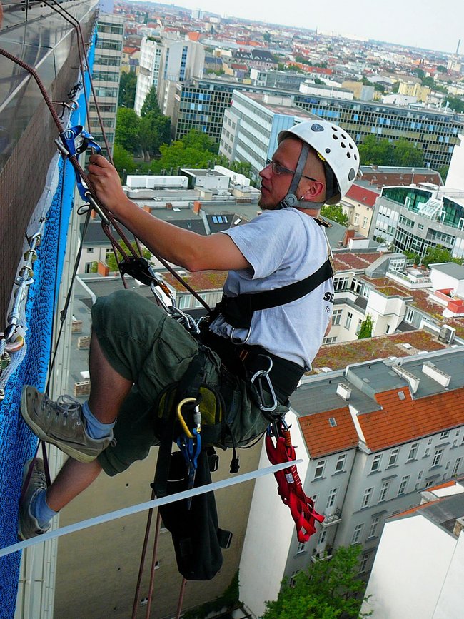 Ein Mann mit Sicherheitsausrüstung arbeitet an der Außenwand eines Hochhauses.