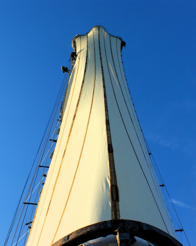 Ein hoher Aussichtsturm mit einer hellen, segelartigen Verkleidung unter blauem Himmel.