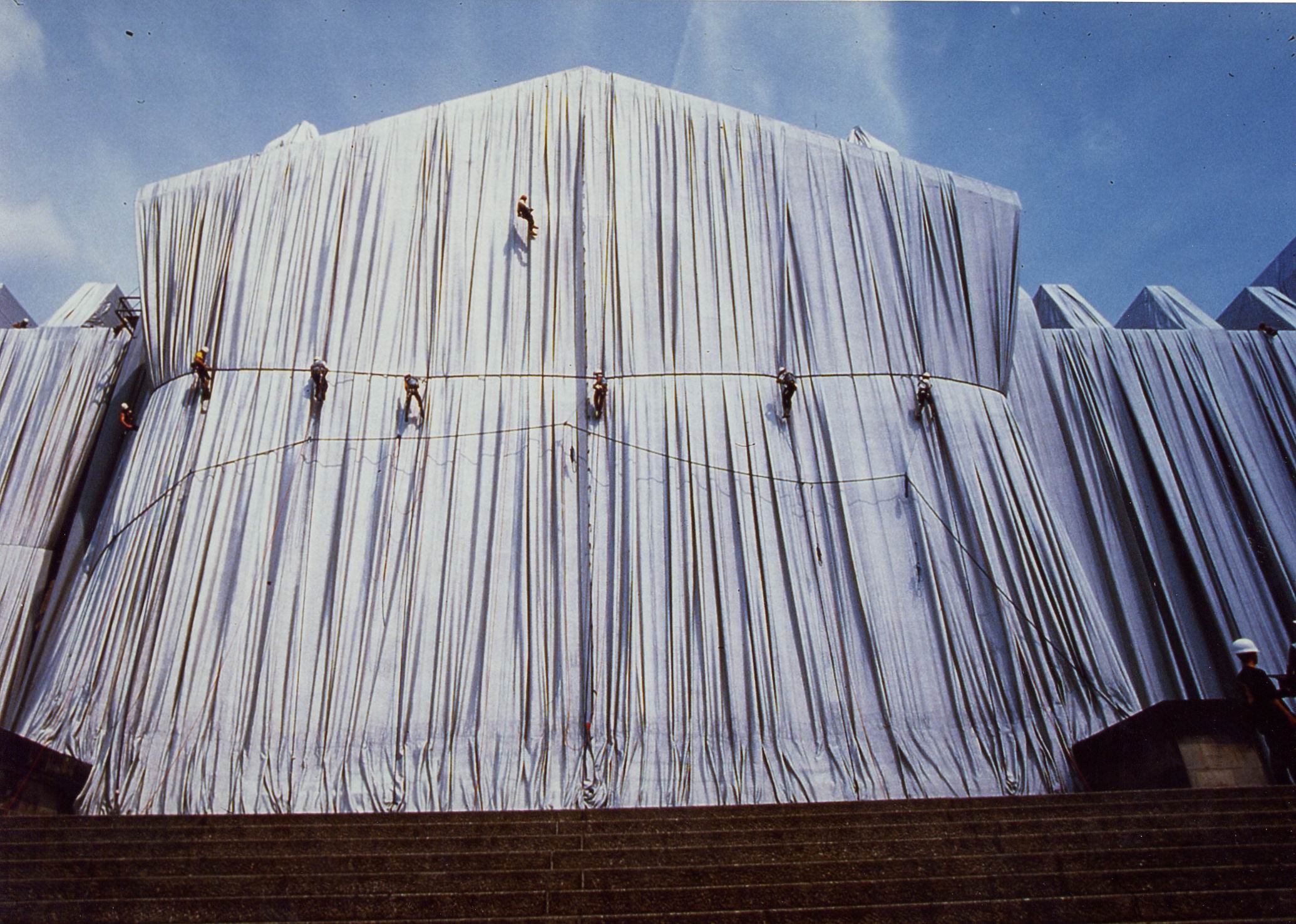 Ein Industriekletterer von ZITRAS beim Klettern an einer mit weißem Stoff verhüllten Gebäudestruktur, möglicherweise am Reichstag, um die Expertise des Unternehmens in Höhenarbeit zu demonstrieren